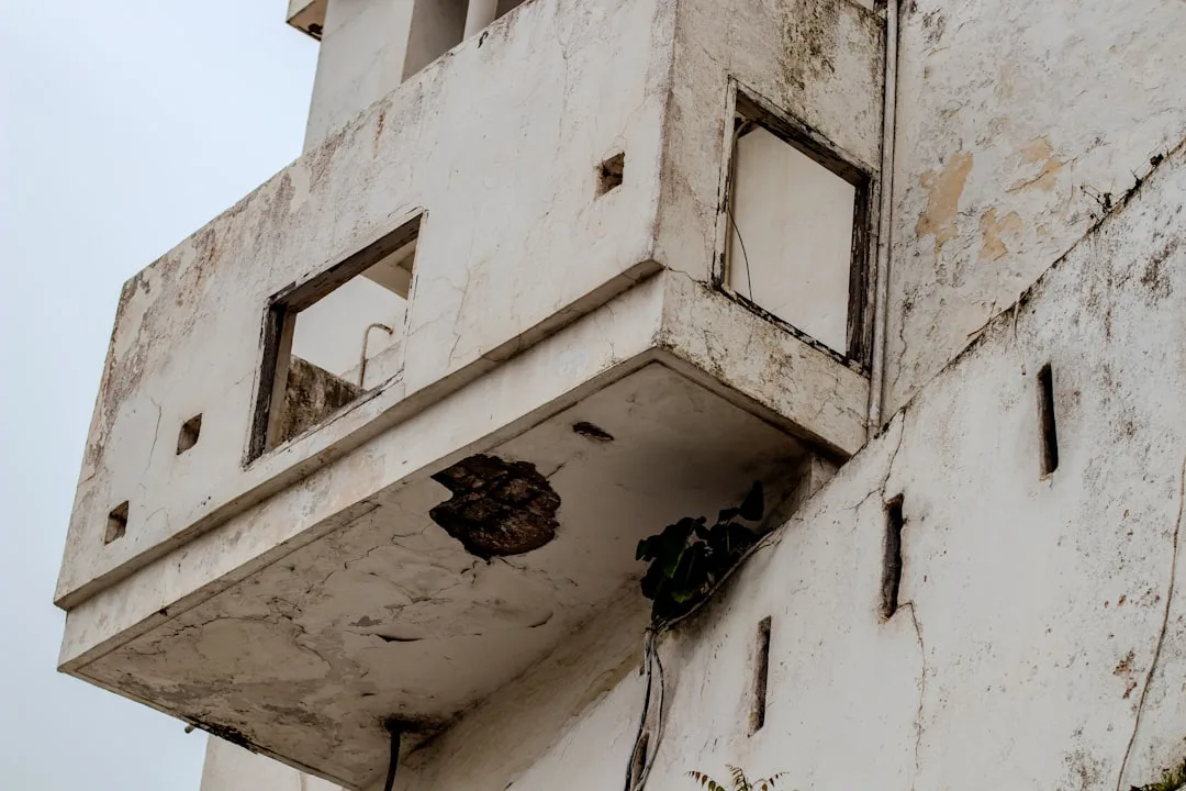 A dilapidated white building with a damaged balcony