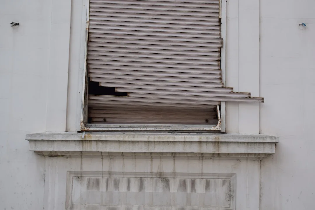A broken window shutter on a white building facade.